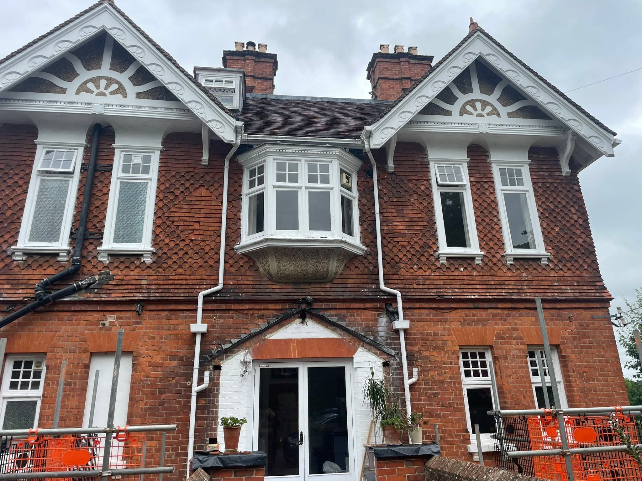 Victorian red brick house with ornate white gables, scalloped tiles, and a central bay window.