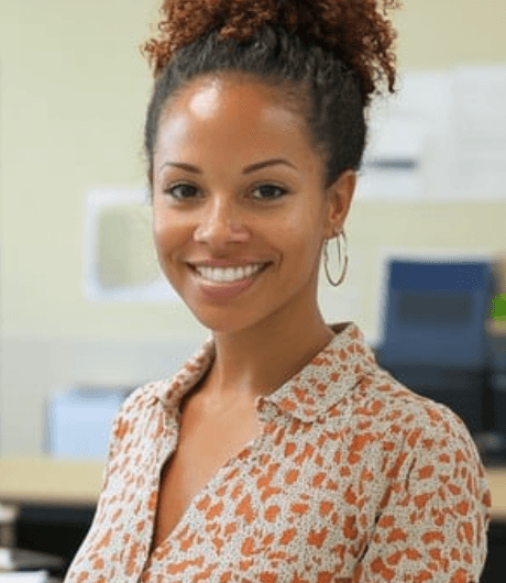 Smiling woman with curly hair in a bun, wearing a patterned blouse and hoop earrings.
