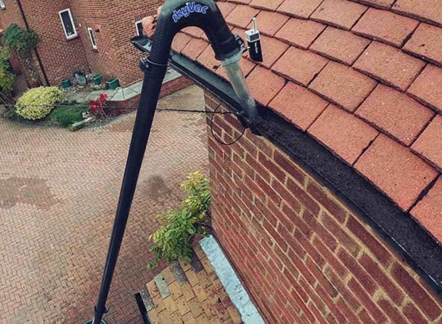 Long black vacuum pole with a curved nozzle cleaning debris from a brick house gutter.